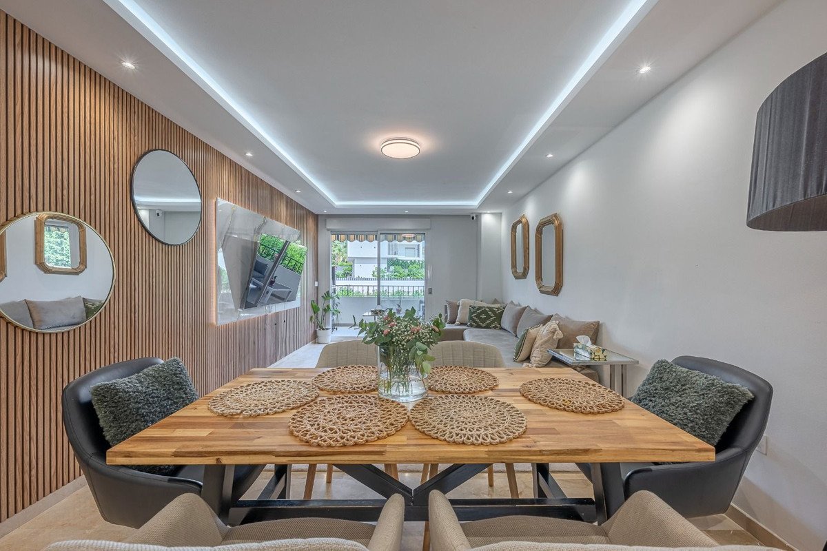 Modern open-plan dining and living room with wooden table, seating, and large windows.