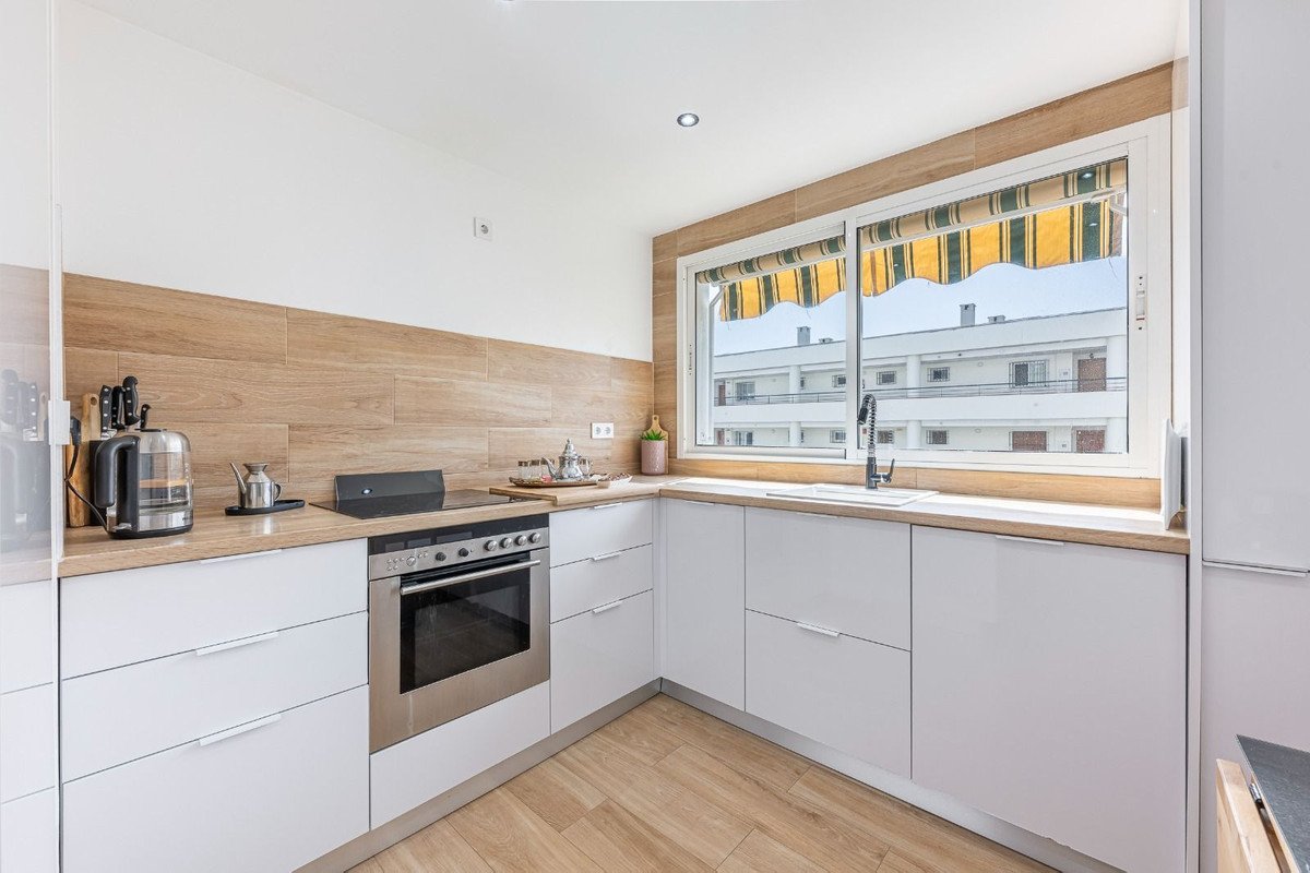 Modern kitchen with white cabinets, wooden backsplash, and a window showing an apartment view.