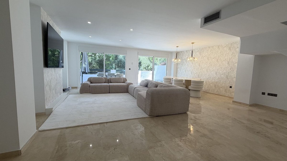 Spacious modern living and dining area with a sectional sofa, large rug, and stylish pendant lights, opening to an outdoor view.