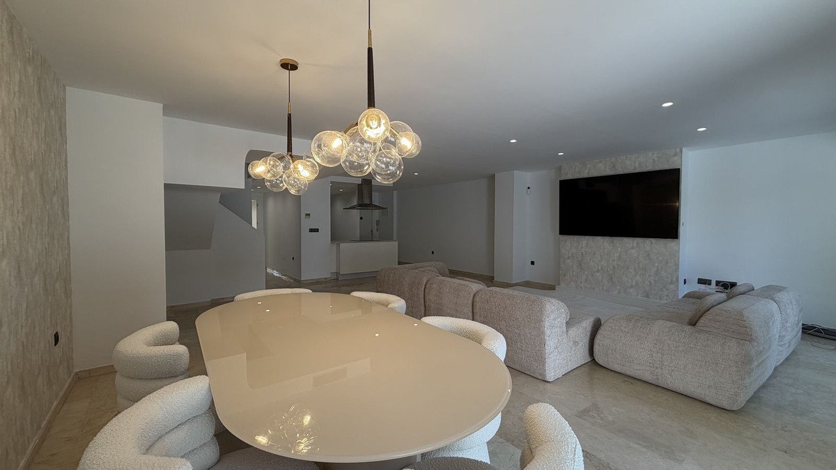 Spacious open-plan living and dining area with modern furniture, a large TV, and stylish pendant lights.
