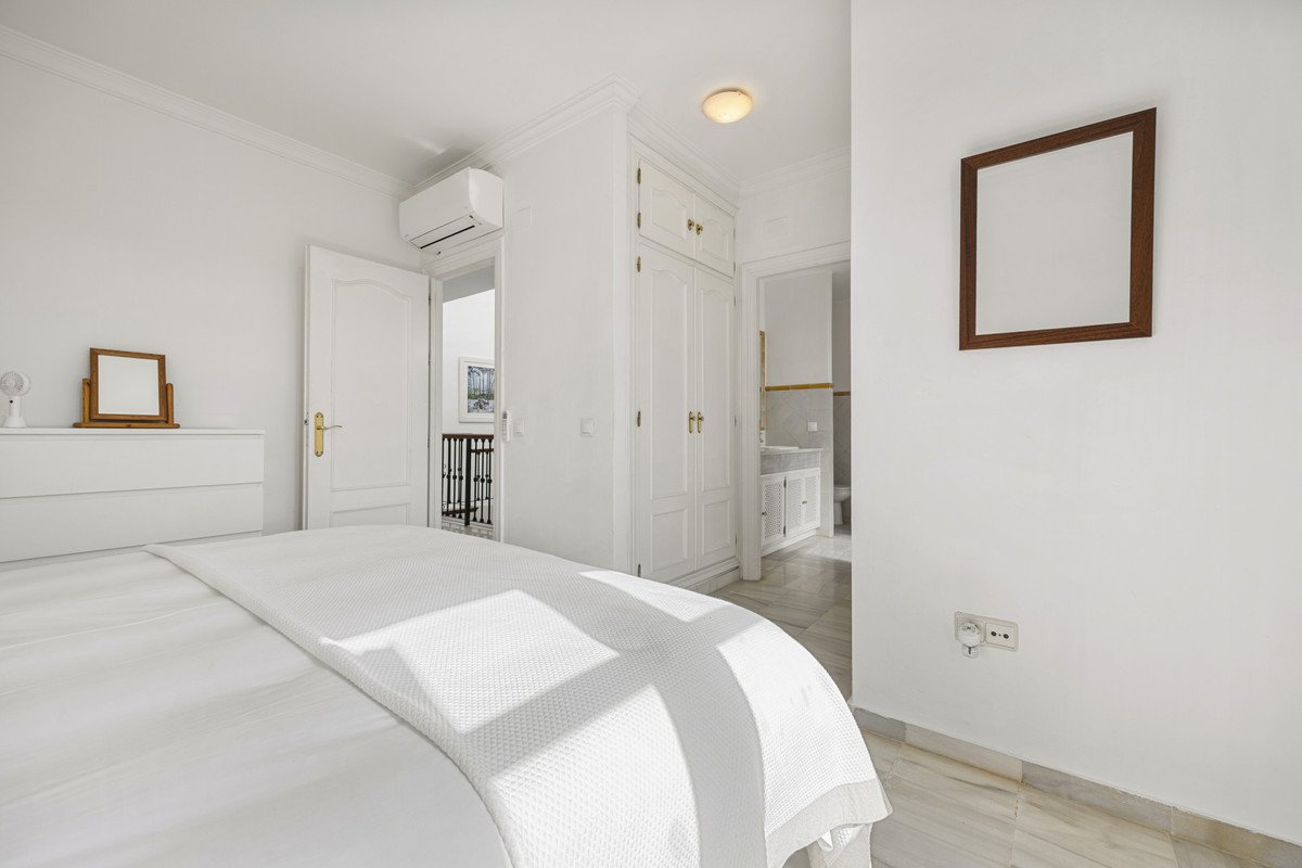 Bright white bedroom with a bed, dresser, and view of a balcony and bathroom.