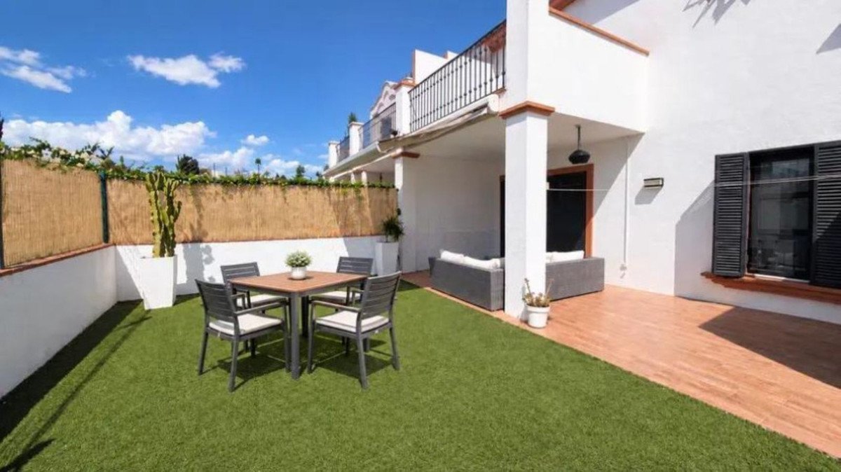 Terrace with artificial grass, dining table and chairs, and an outdoor lounge area under a covered patio.