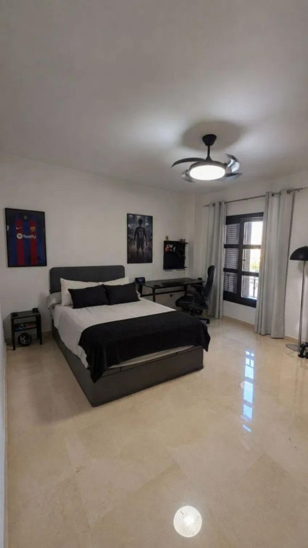 Modern bedroom with a double bed, desk with chair, and a window with black shutters, decorated with sports posters.