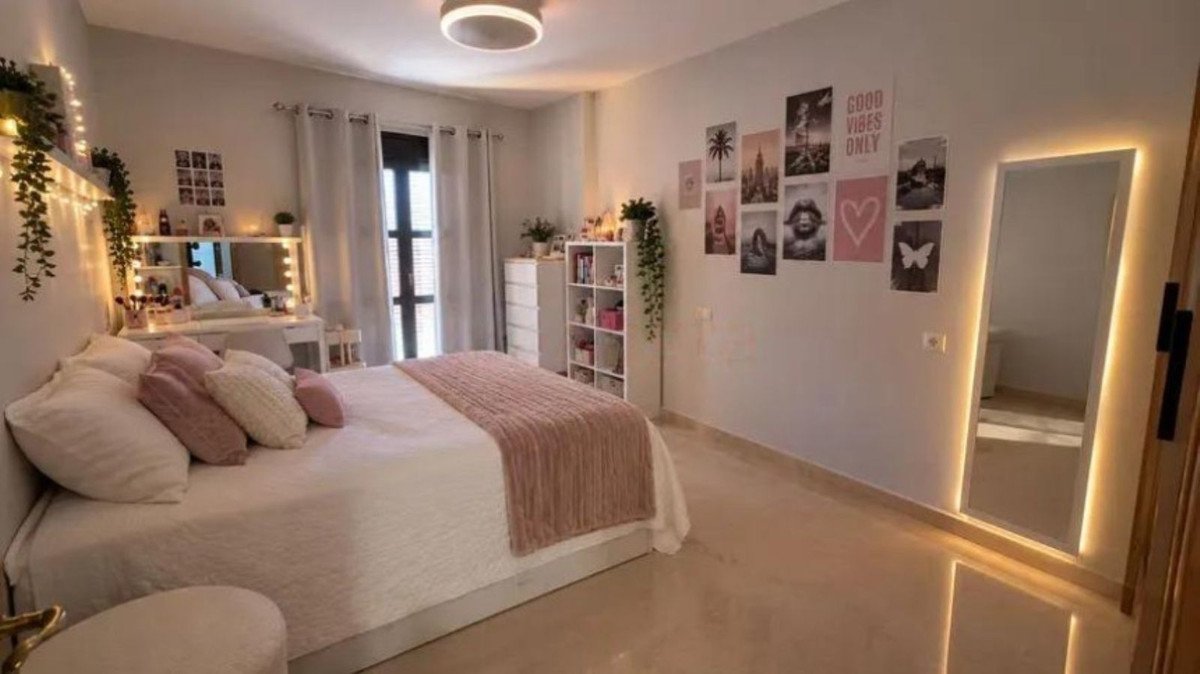 A stylish bedroom with a bed, vanity desk with lights, and a large illuminated mirror on-trend mirror with LED lighting.