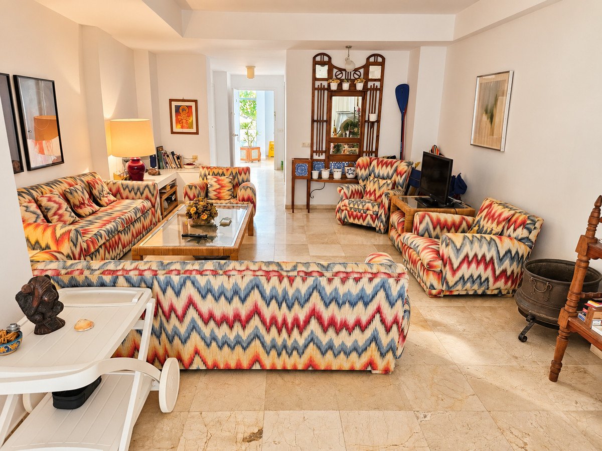 Colorful living room with sofas, armchairs, and a glass coffee table, bathed in natural light.