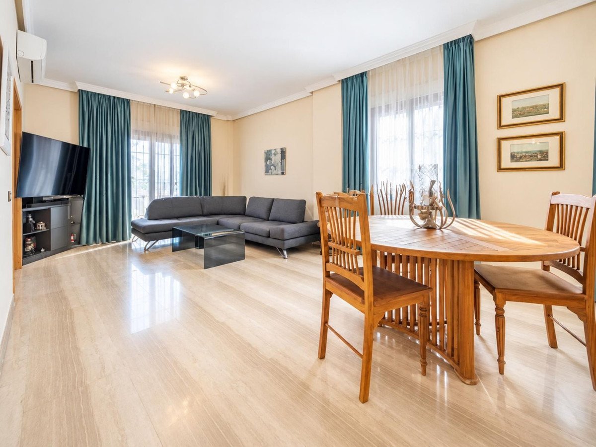 Spacious living and dining area with a sectional sofa, coffee table, dining table, and chairs, featuring large windows and bright natural light.