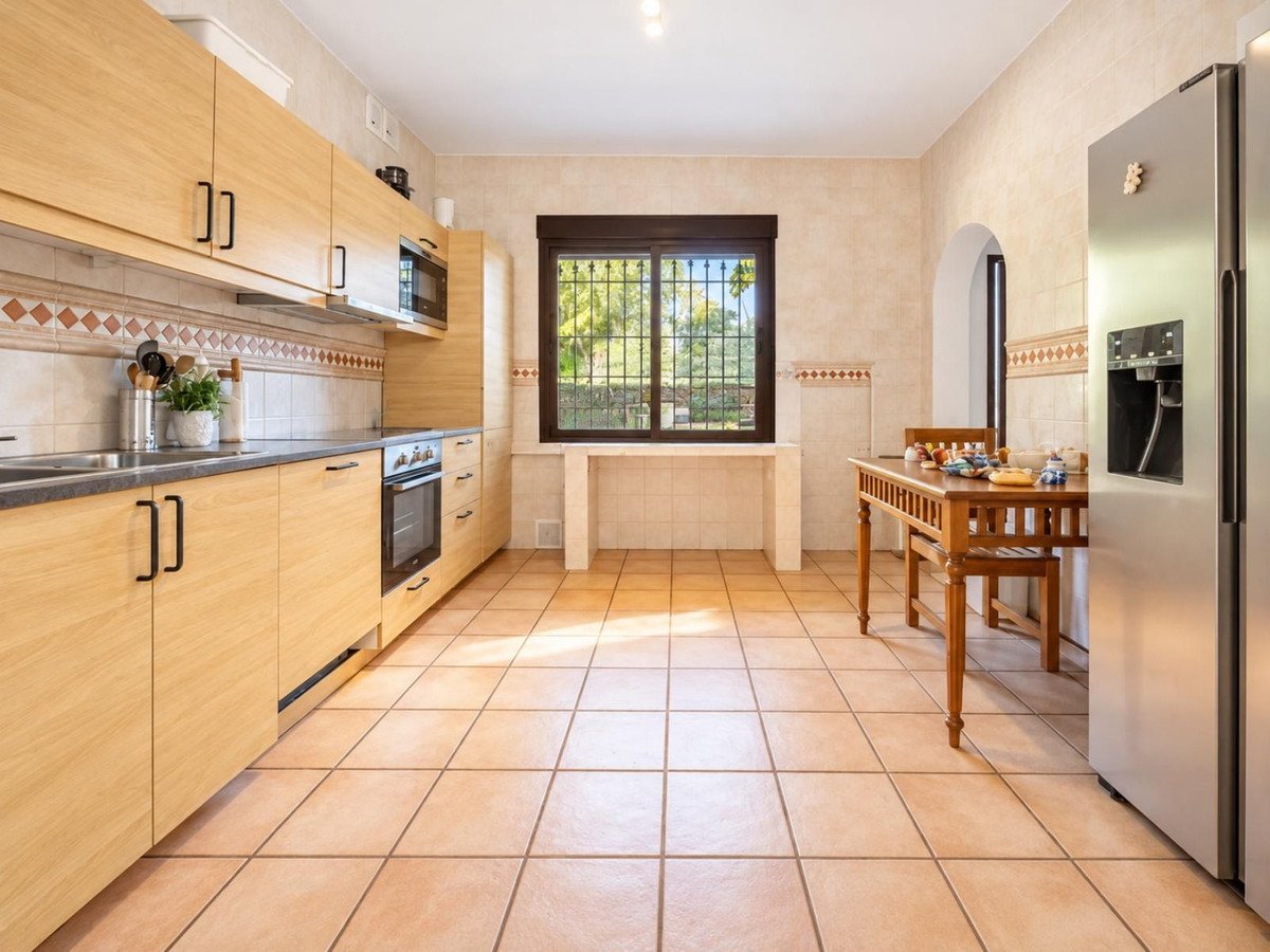 A spacious kitchen featuring light wood cabinets, stainless steel appliances, a dining table, and a window with a view of greenery.