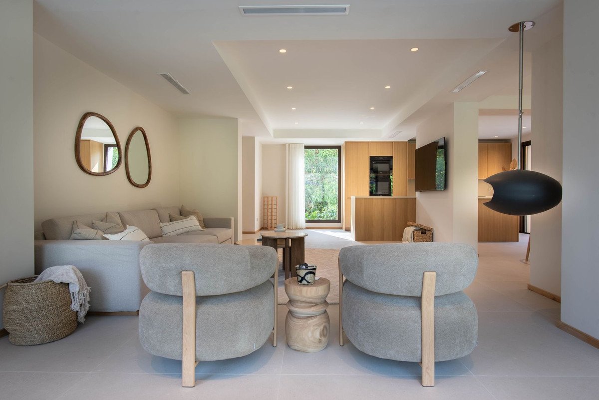 Modern living room with comfortable seating, a sleek kitchen, and a unique hanging fireplace with a view of lush greenery.