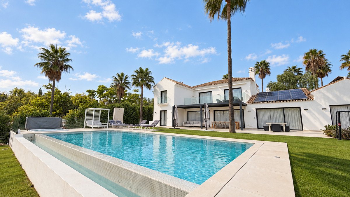 Modern white villa with swimming pool, palm trees, and outdoor seating under sunny sky