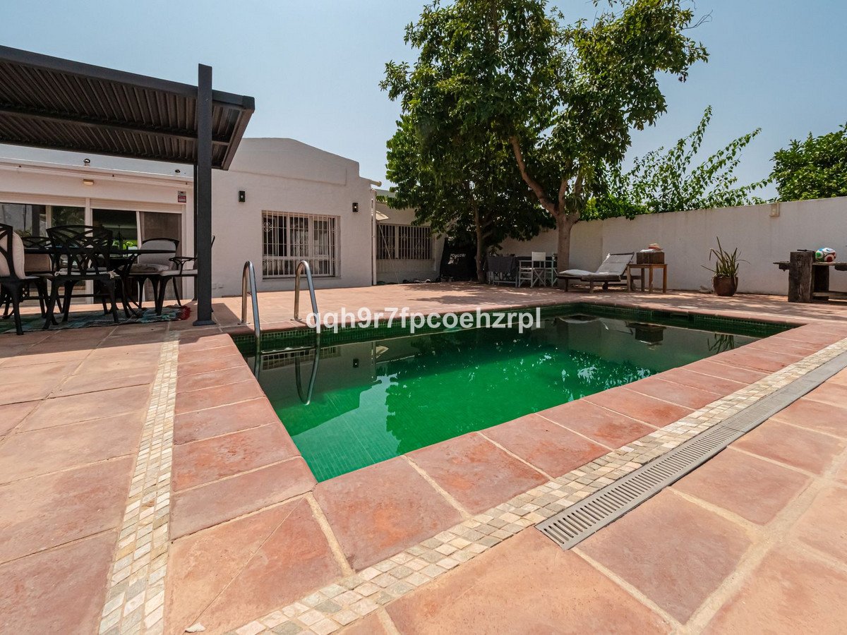 A patio with a swimming pool and outdoor seating area, shaded by trees and a pergola.
