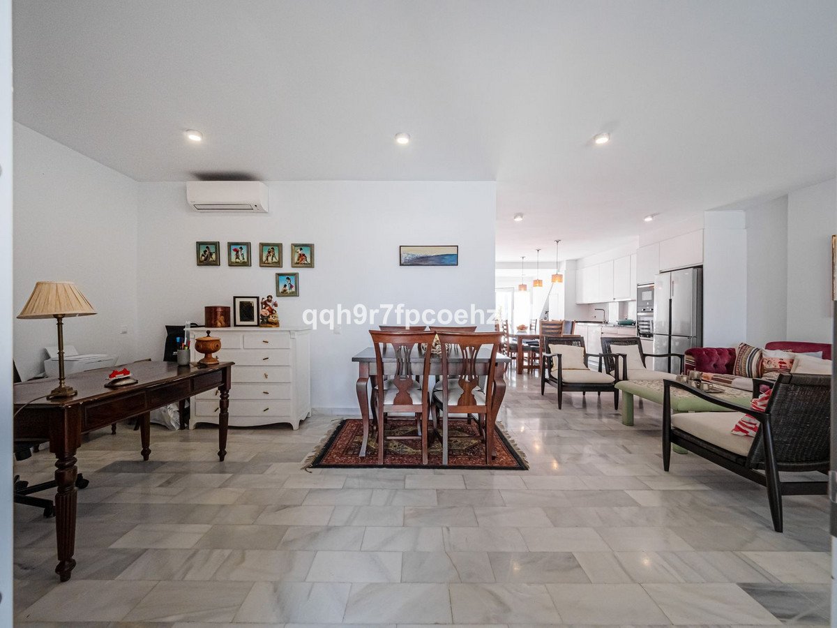 Open-plan living and dining area with a kitchen in the background and marble floors.