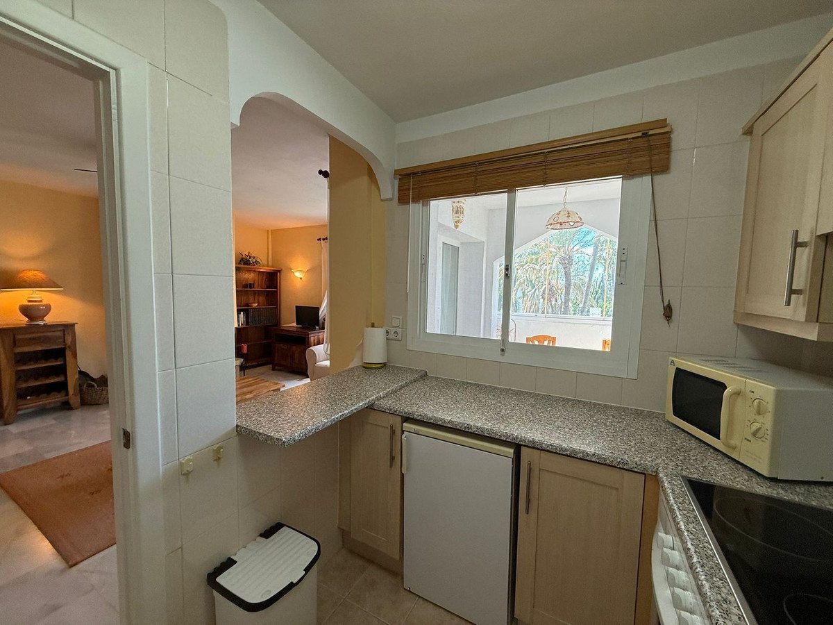 Kitchen area with speckled countertops, white cabinets, microwave, and a window with a view of a terrace and palm trees.