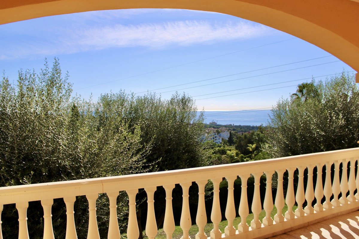 Balcony with white railing overlooking green hills and the sea
