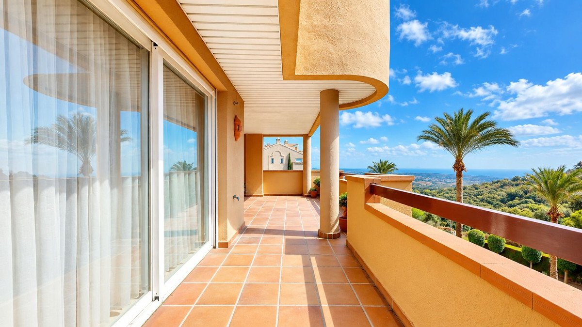 Spacious terrace with tiled floor, large glass doors, offering a scenic view of the sea and palm trees.