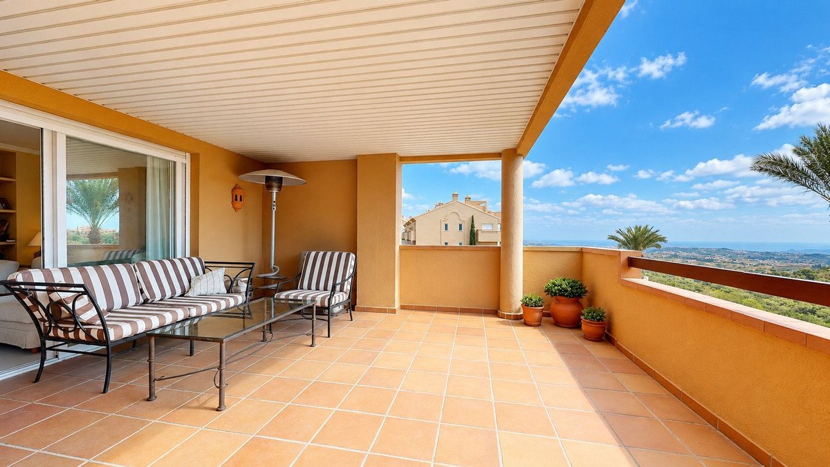 Spacious covered terrace with outdoor seating and panoramic sea and landscape views under a blue sky.