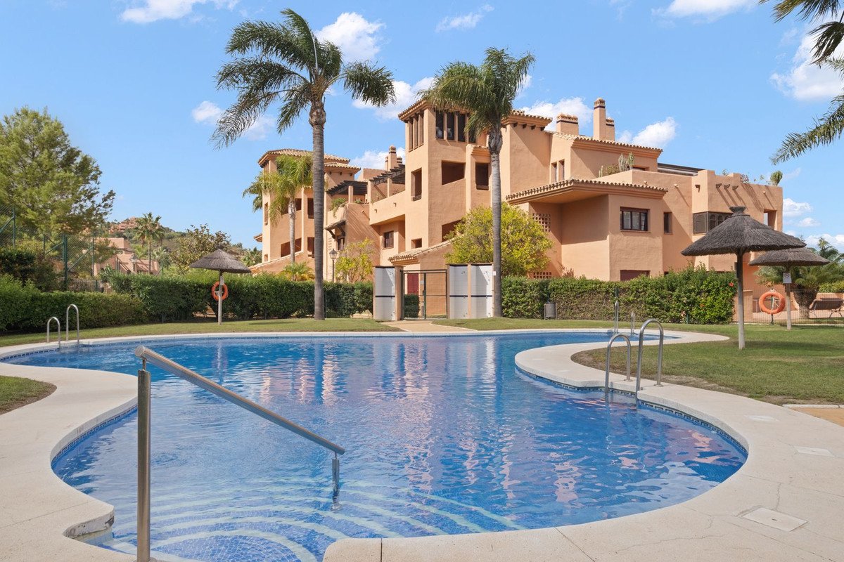 A freeform swimming pool with steps and railings in the foreground, and an apartment complex with palm trees and gardens in the background.