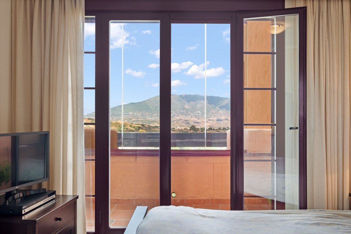 Bedroom with large balcony doors opening to a view of mountains and a bright blue sky with clouds.