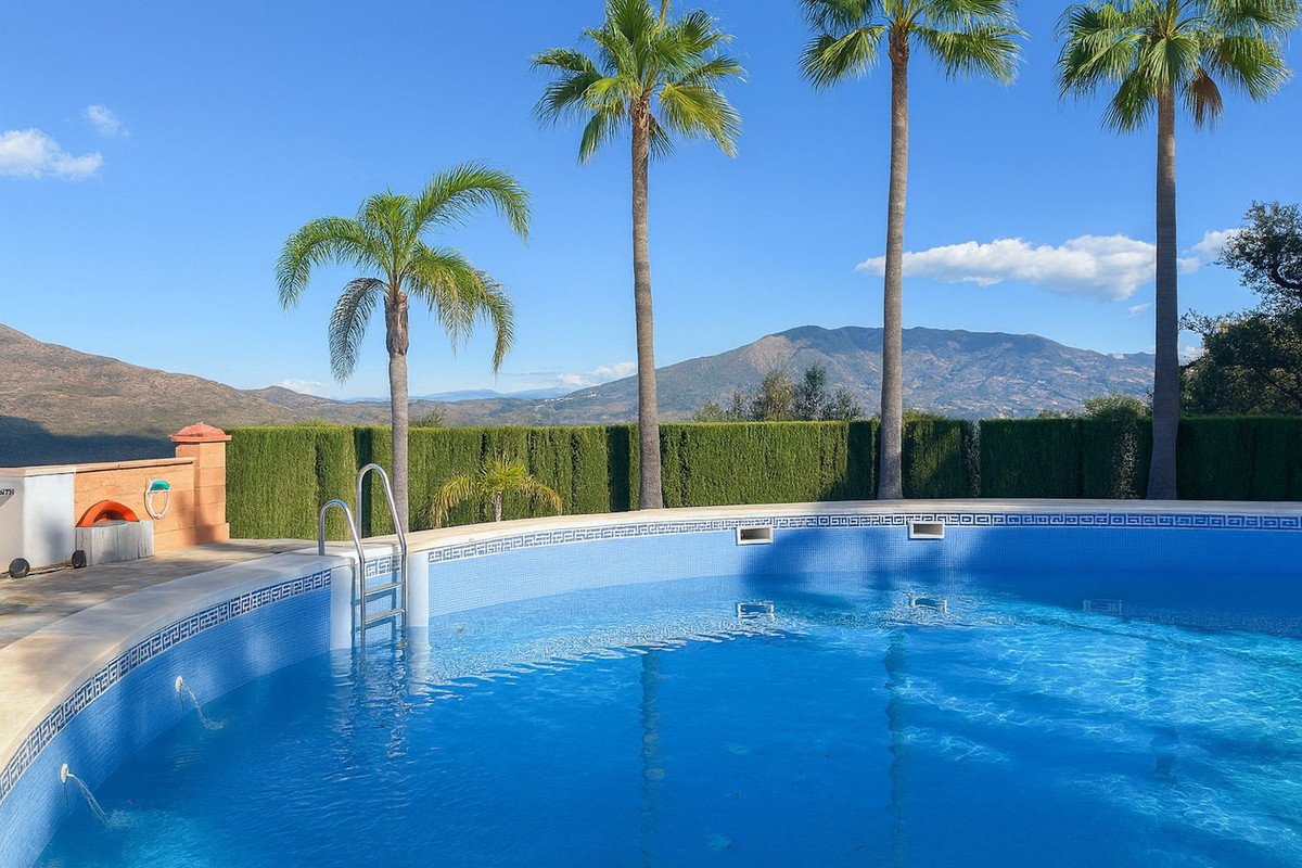 Villa with private pool, palm trees, and mountain views under a clear blue sky.