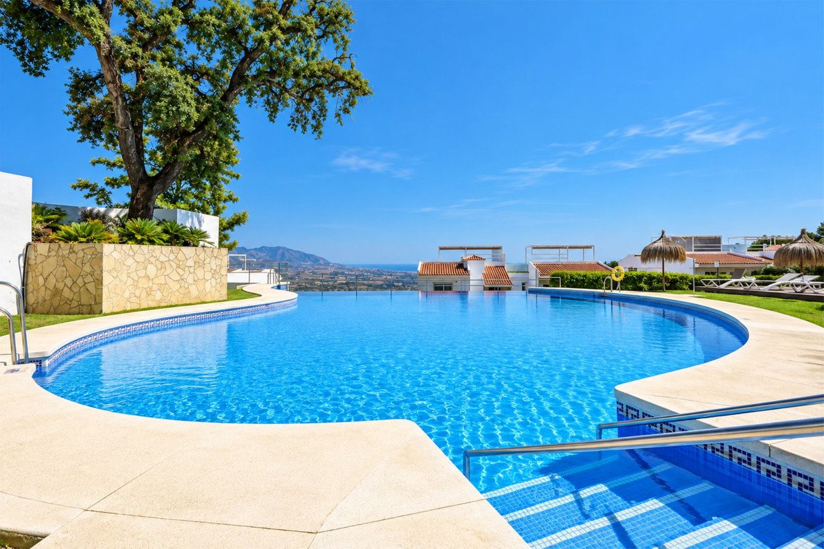 Large infinity swimming pool with steps and surrounding lounge area offering panoramic sea and mountain views under a clear blue sky.