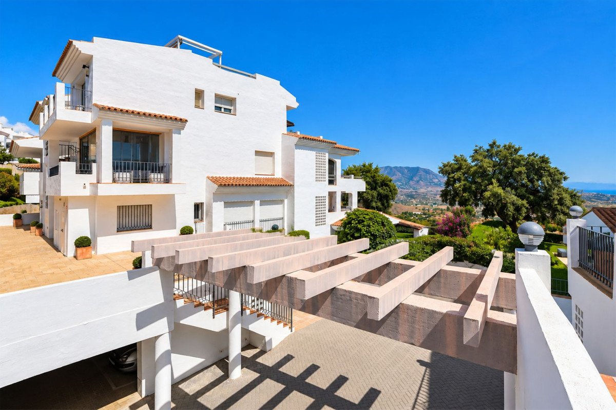 White villa with balconies and a pergola, overlooking a verdant landscape with mountains and the sea in the distance.