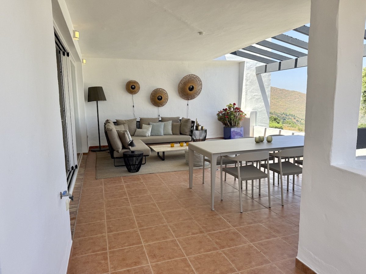 Modern covered terrace with comfortable lounge seating, dining table, and scenic hillside views.