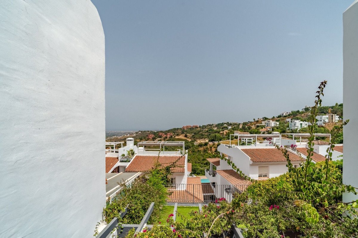 View of several villas with terracotta roofs on a hillside, with lush greenery and a distant hazy view.