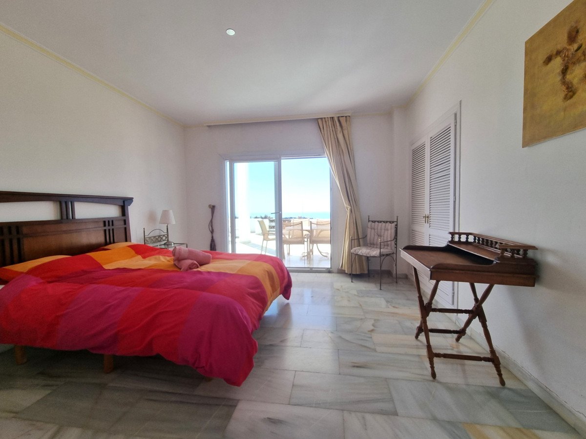 A bedroom with a colorful duvet, balcony doors opening to a terrace with sea view and outdoor seating.