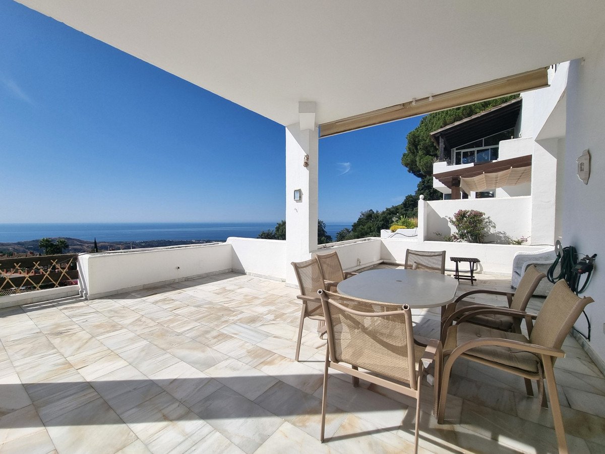 Spacious tiled terrace with dining table and chairs overlooking a beautiful sea view and surrounding hills.