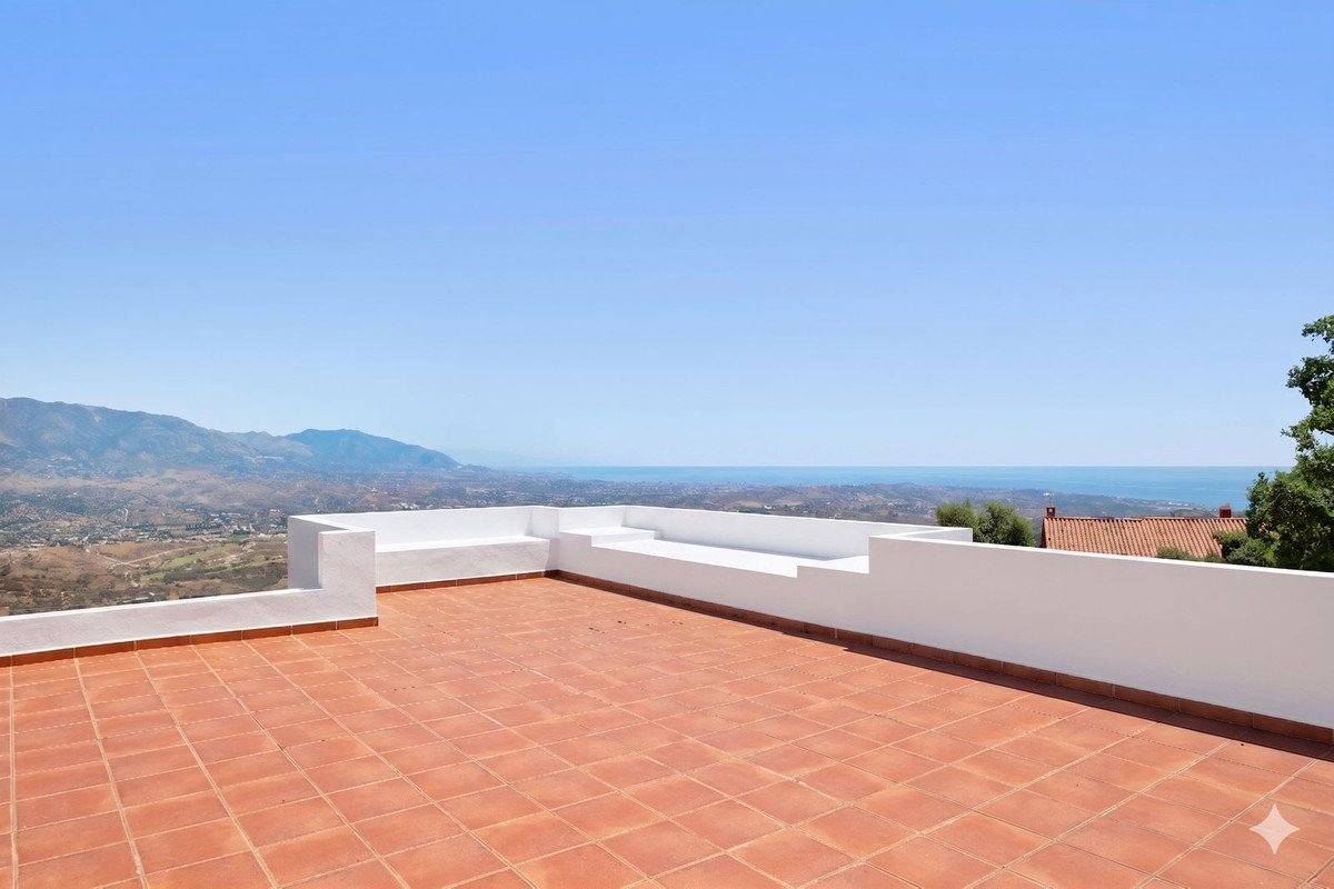 Spacious tiled terrace with built-in seating and panoramic views of the sea and mountains under a clear blue sky.