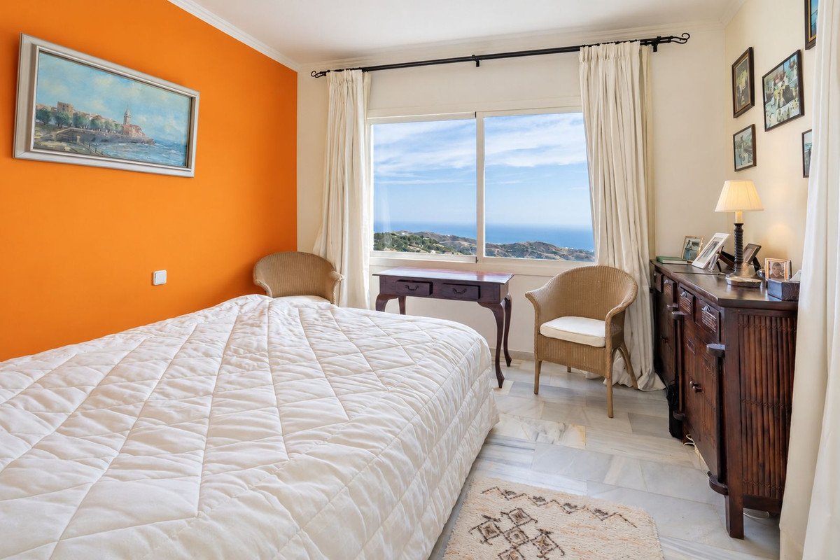 Bedroom with a large window offering a sea view, orange accent wall, and rattan chairs.