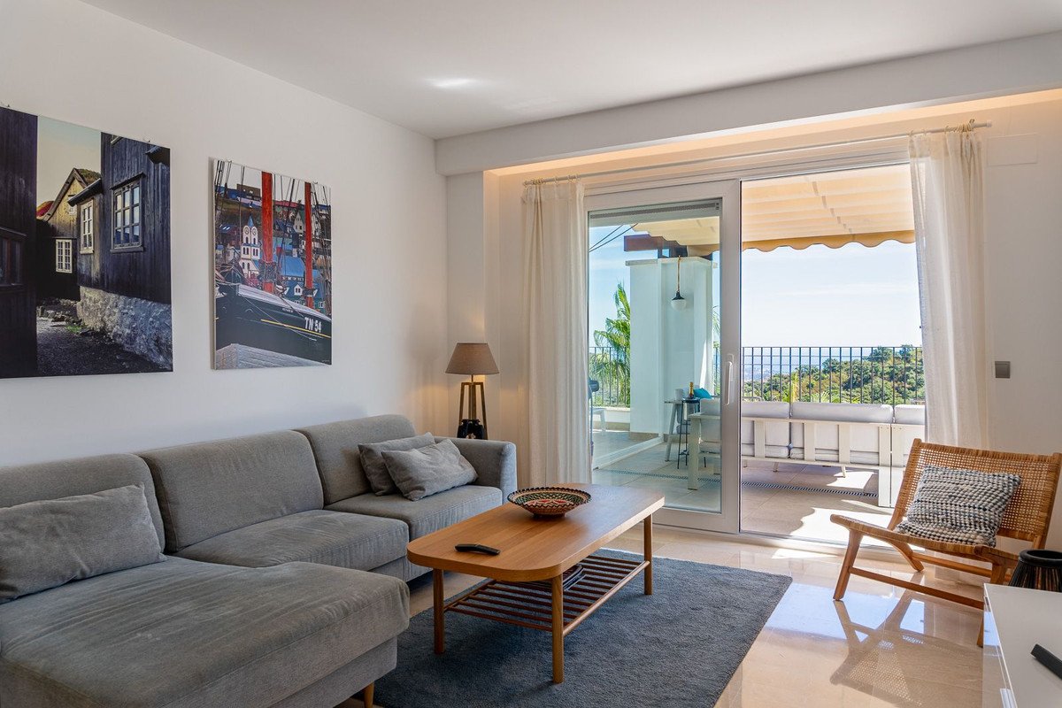Comfortable living room with a large sofa, coffee table, and balcony access offering a beautiful sea view and lush greenery.
