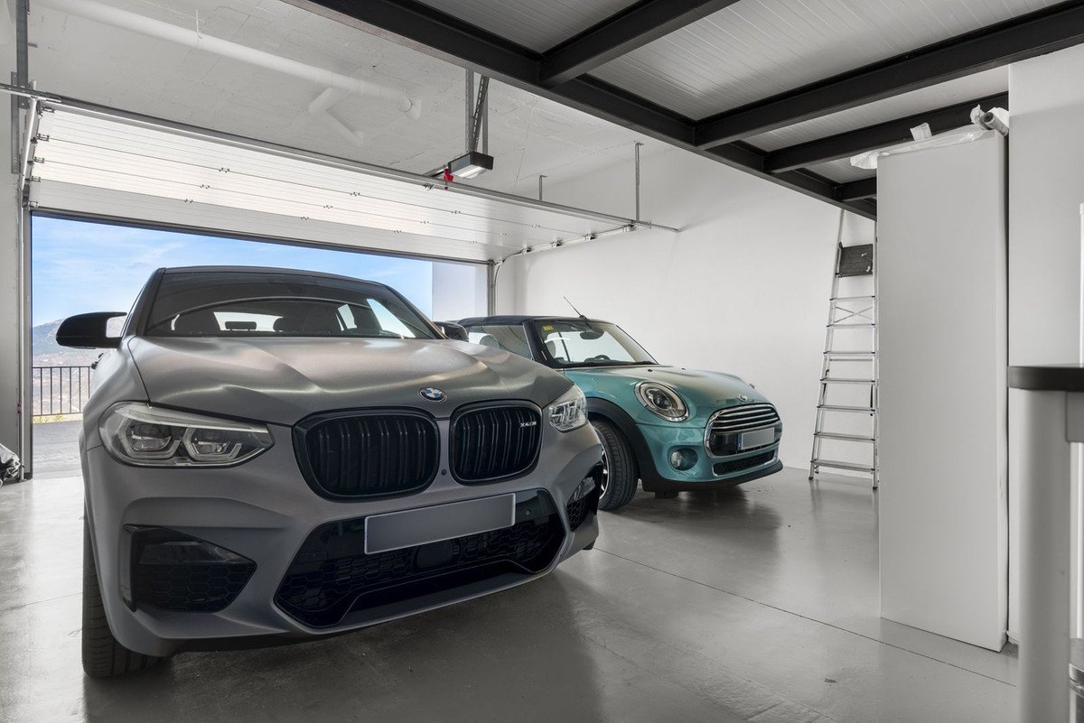 Modern garage with two cars, open door, and ladder.
