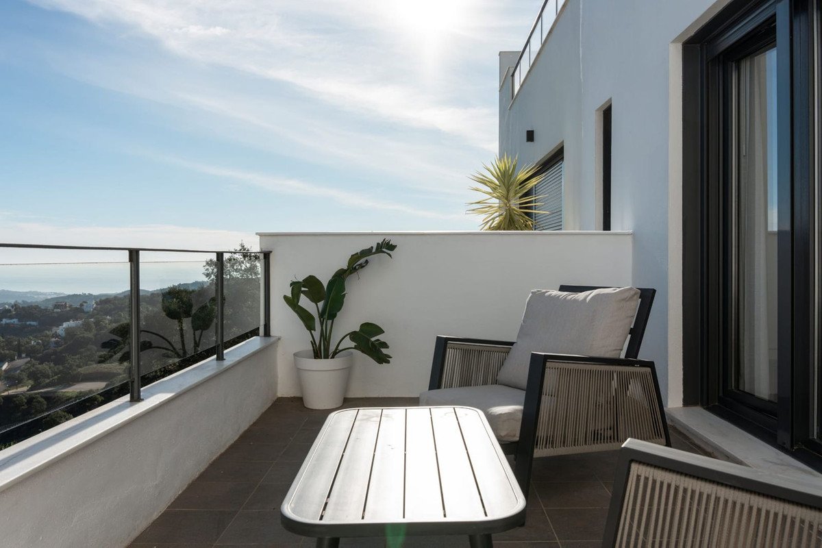 Modern balcony with comfortable seating, coffee table, and a panoramic view of the sea and hills under a clear sky.