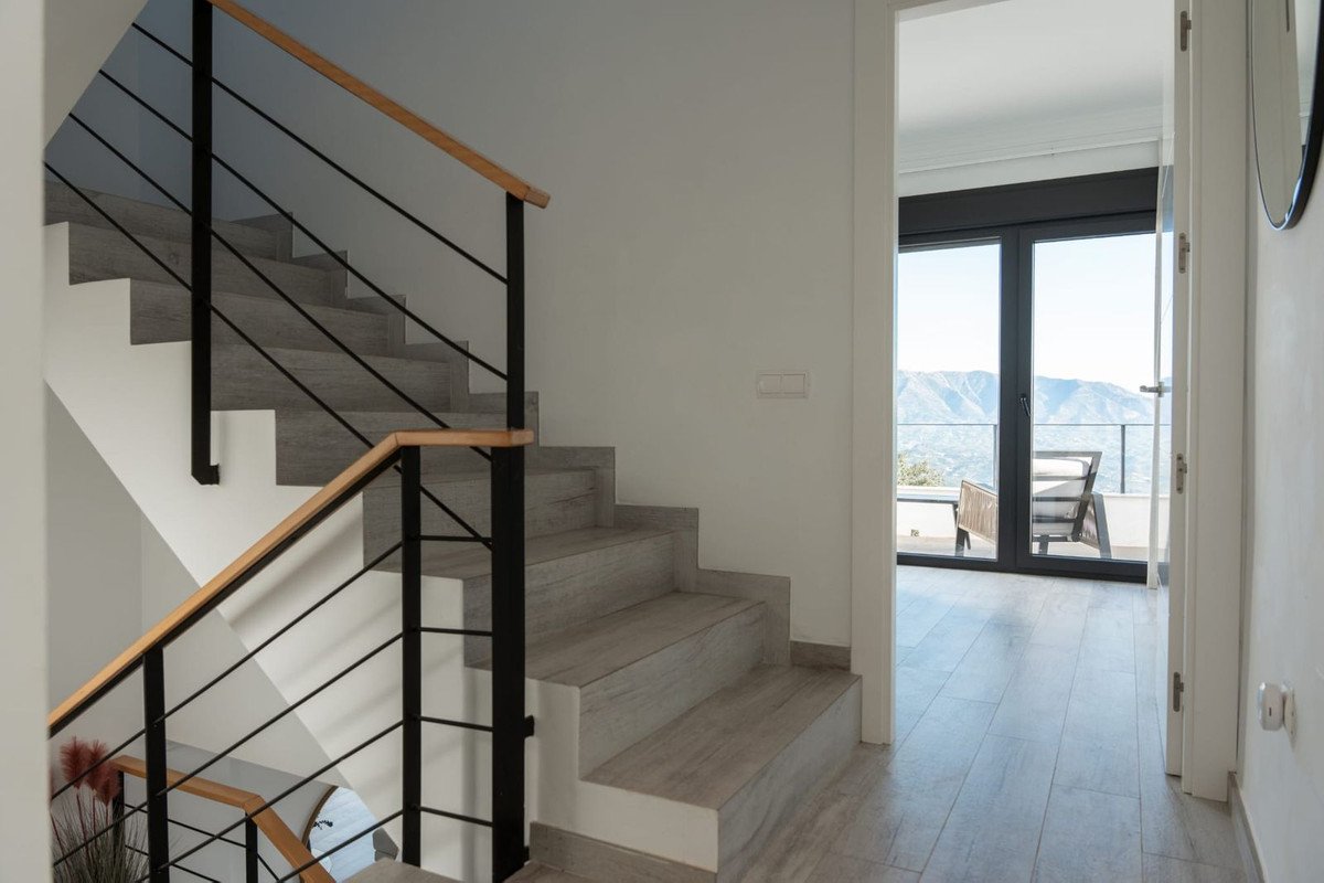 Modern staircase with wooden handrail and black railings, leading to a balcony with mountain views.