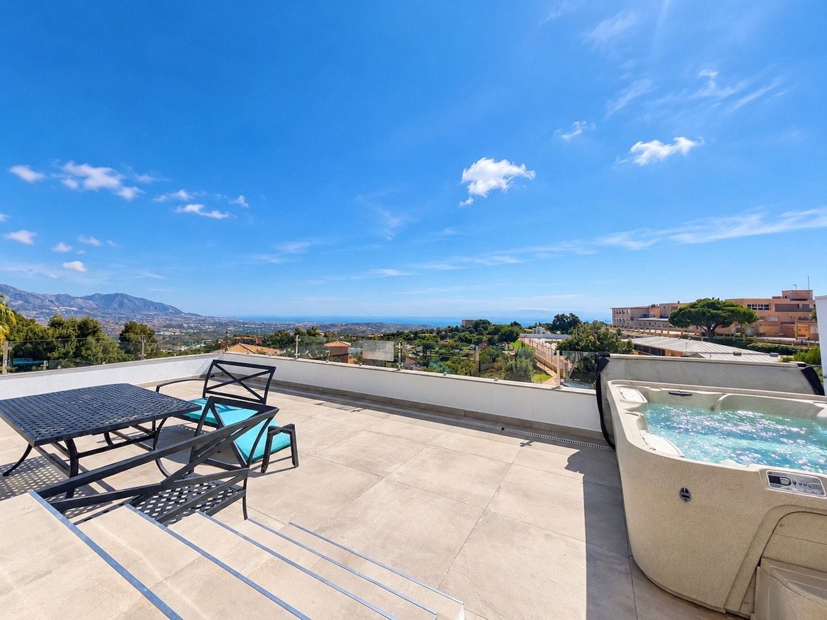 Terrace with a jacuzzi, dining table and chairs, overlooking a scenic sea and mountain view under a clear blue sky.