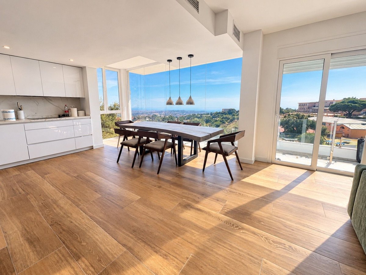 Modern dining area with kitchen, wooden floors, and panoramic outdoor view