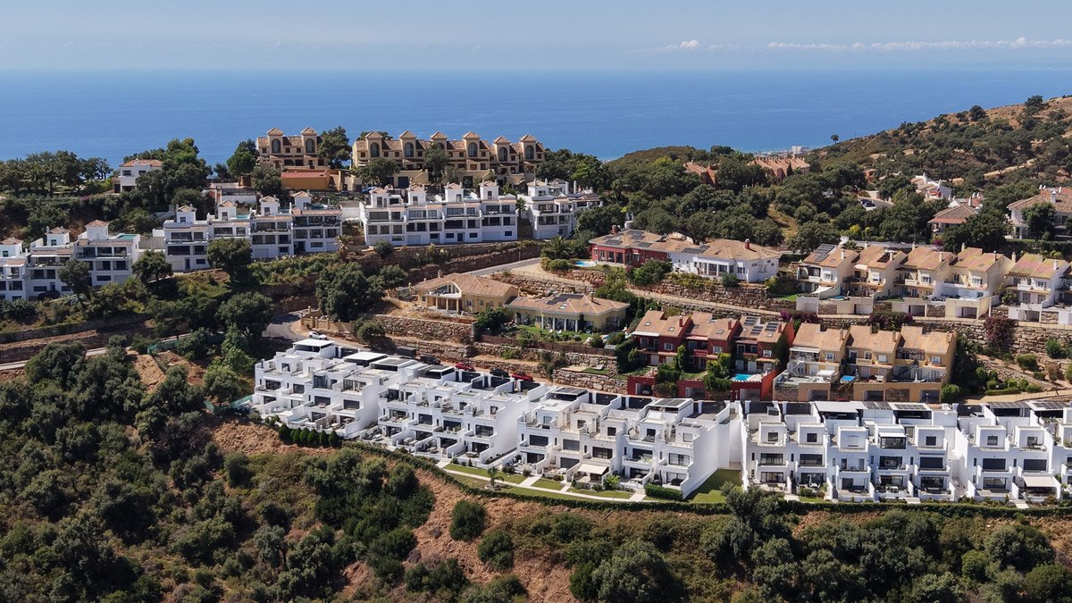 Modern white apartment complex nestled on a hillside, offering sea views and lush green surroundings.