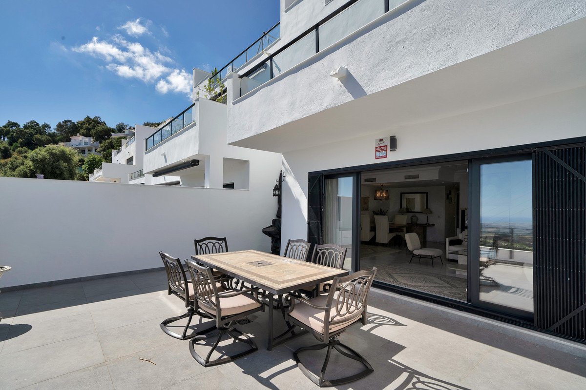 Terrace with a dining set overlooking the sea, with an open sliding door leading to a modern interior.