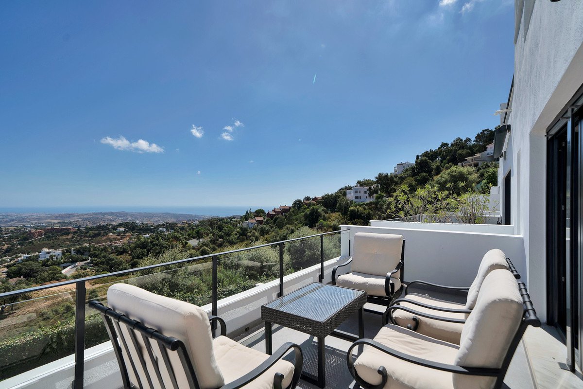 Terrace with seating and table overlooking a scenic mountain landscape with the sea in the distance on a sunny day.