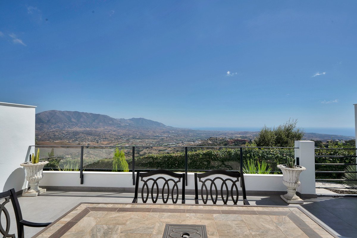 Terrace with two ornate chairs overlooking a valley, mountains, and the sea under a clear blue sky.