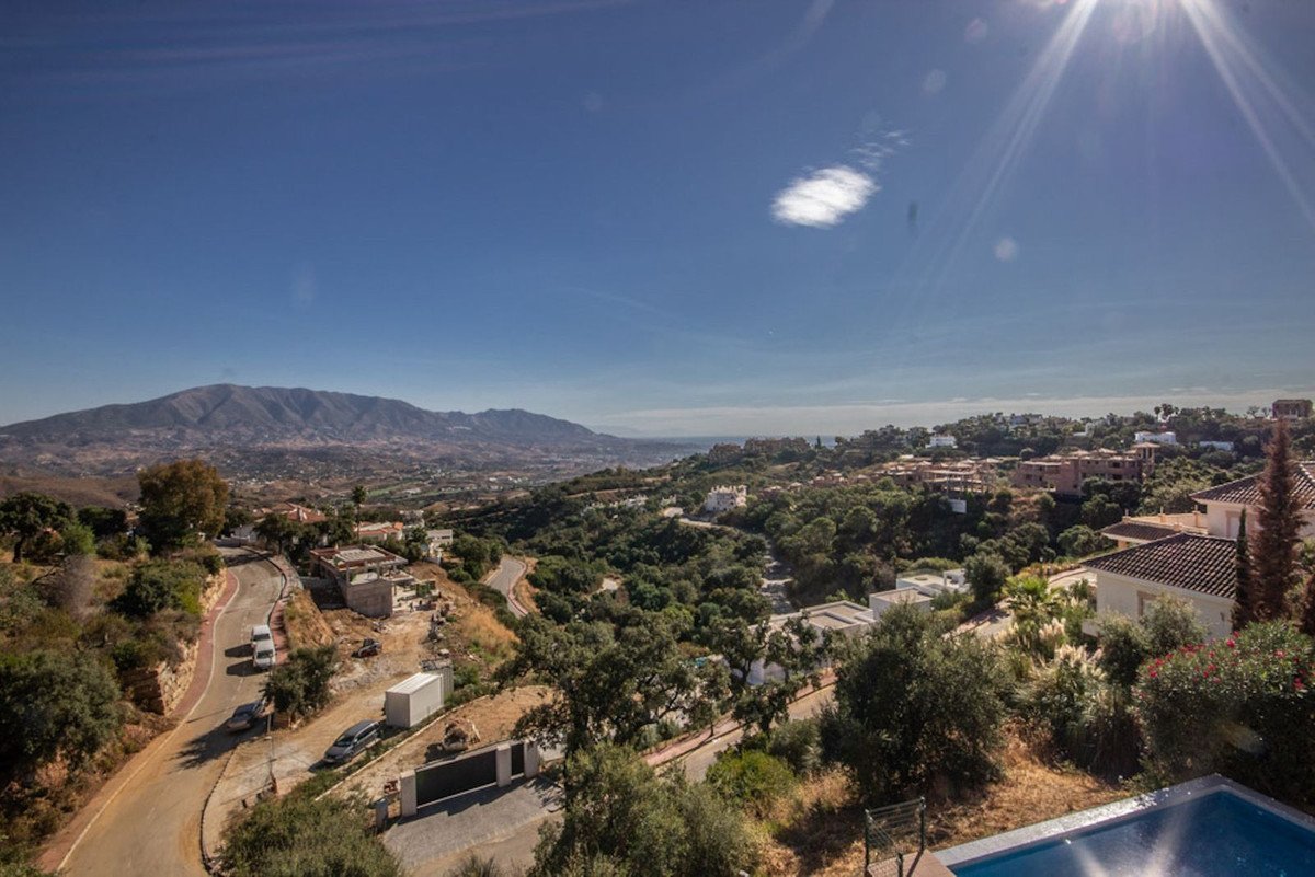 Panoramic view from a villa balcony overlooking mountains, the sea, and a lush green landscape with scattered houses.