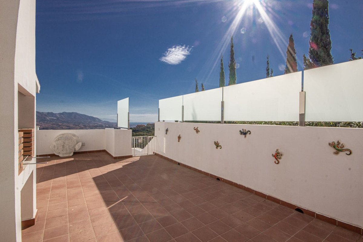 A spacious terrace with a built-in grill and a white circular chair, offering a panoramic view of the sea and mountains under a sunny sky.