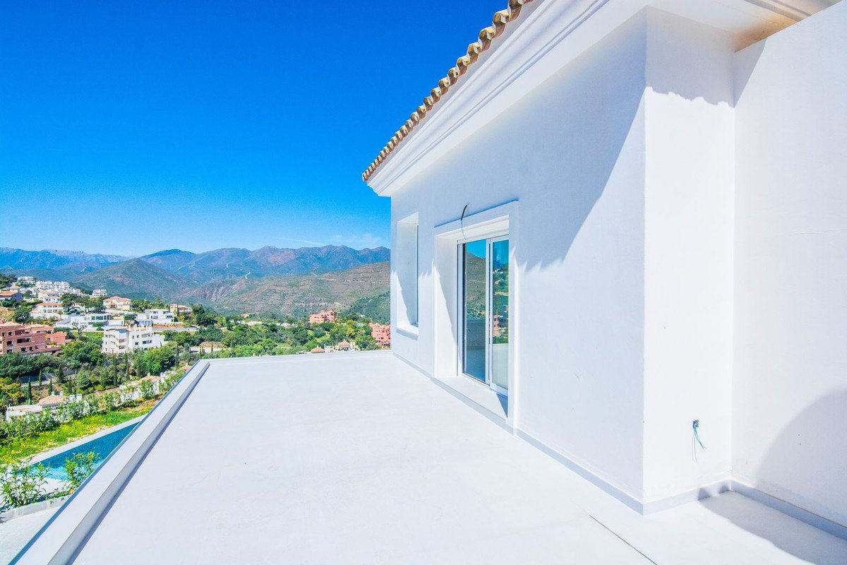 White modern terrace with a stunning mountain and town view, overlooking a private swimming pool on a sunny day.