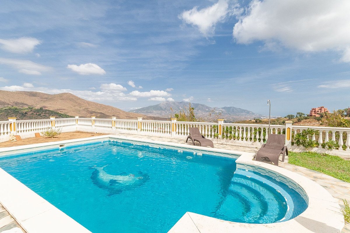 A swimming pool with a dolphin mosaic on the bottom, chaise lounges, and a scenic view of mountains and a town below.
