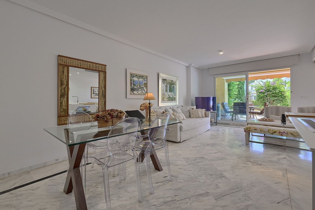 Spacious living and dining area with a glass table, sofa, and terrace access with garden view.