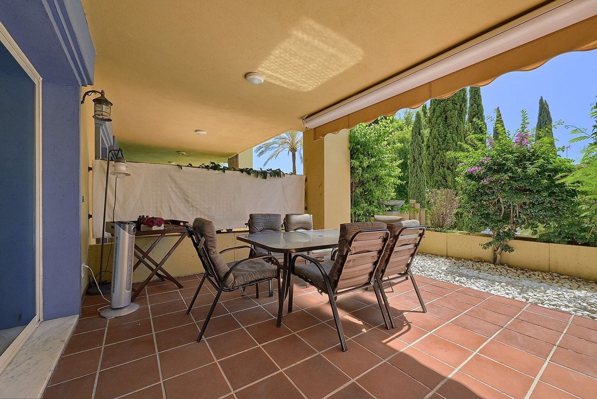 Covered terrace with dining set and chairs, overlooking a lush green garden with trees and flowers.