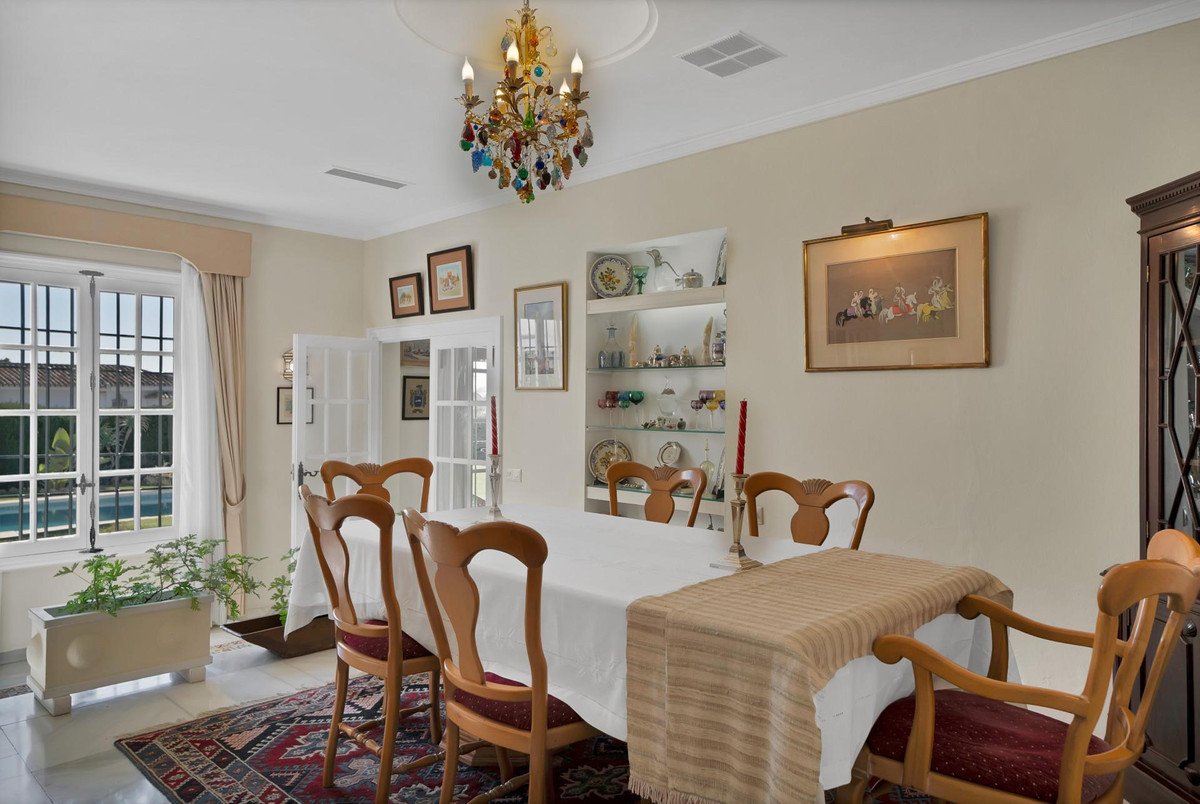 Formal dining room with a large table, chairs, chandelier, and a view of a swimming pool through the window.