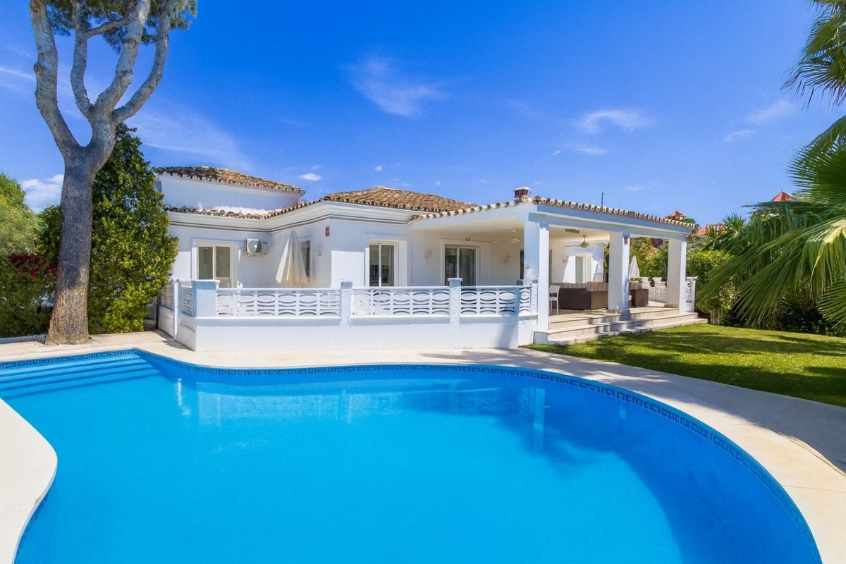 A white villa with a blue swimming pool and a covered terrace with outdoor seating.