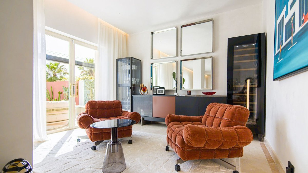 Modern living room with two orange velvet armchairs, a glass coffee table, a wine cooler, and a view of a patio.