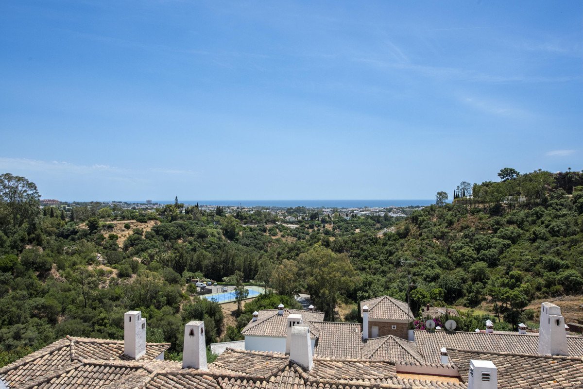 A scenic view of rolling green hills, a distant town, the sea, and a resort swimming pool under a clear blue sky.